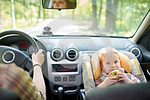 Young beautiful woman driving a car. On a front seat mounted child safety seat with a pretty 1 year old toddler boy. Child