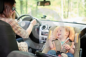 Young beautiful woman driving a car. On a front seat mounted child safety seat with a pretty 1 year old toddler boy. Child