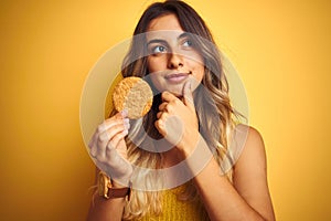 Young beautiful woman eating biscuit over grey isolated background serious face thinking about question, very confused idea