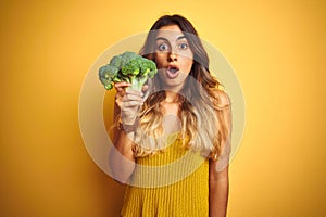 Young beautiful woman eating broccoli over yellow isolated background scared in shock with a surprise face, afraid and excited