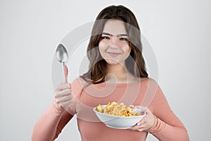 Young beautiful woman eating corn flakes with milk looking hungry standing on isolated white background, healthy breakfast concept