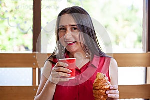 Young beautiful woman eating croissant and drinking coffee