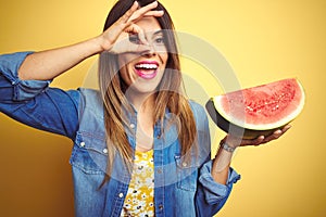 Young beautiful woman eating fresh healthy watermelon slice over yellow background with happy face smiling doing ok sign with hand