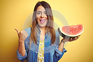 Young beautiful woman eating fresh healthy watermelon slice over yellow background pointing and showing with thumb up to the side