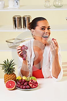 Young beautiful woman eating grapes from a fruit bowl