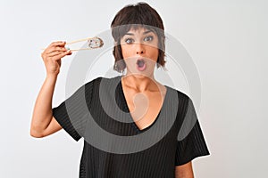 Young beautiful woman eating sushi using chopsticks standing over isolated white background scared in shock with a surprise face,