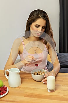 Young beautiful woman eats breakfast cereal with berries and milk