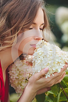 Young beautiful woman enjoying smell of blooming flower on a sunny day