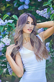 Young beautiful woman enjoying the smell of blooming lilac on a sunny day