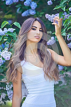 Young beautiful woman enjoying the smell of blooming lilac on a sunny day