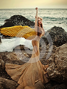 Young beautiful woman fallen angel stands on sea beach enjoy nature. costume bird white wings.