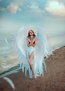 Young beautiful woman fallen angel stands on the sea beach enjoy nature. Creative sexy costume, huge artificial bird