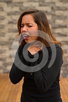 Young beautiful woman feeling bad and gripping her neck, cardiopulmonary resuscitation concept, in a blurred background