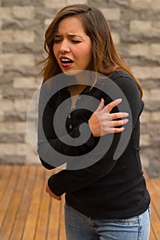 Young beautiful woman feeling bad and touching her arm, cardiopulmonary resuscitation concept, in a blurred background