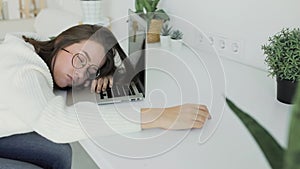 Young beautiful woman fell asleep at a white table in front of a laptop. Side view.
