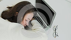 Young beautiful woman fell asleep at a white table in front of a laptop. Top view.