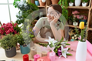 Young beautiful woman florist smiling confident sitting on table at flower shop