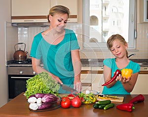 Young beautiful woman and girl making fresh vegetable salad. Healthy domestic food concept. Smiling mother and funny playful daugh