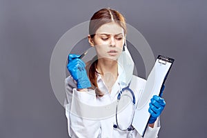 Young beautiful woman in glasses on a gray background in a medical dressing gown holds a pen and documents, medicine, doctor