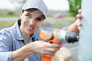 young beautiful woman in gloves uses drill in garden