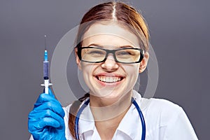 Young beautiful woman on a gray background with glasses holds a syringe, medicine, doctor