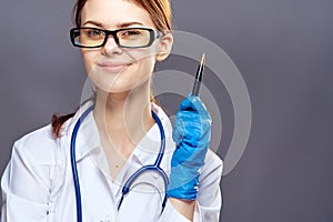 Young beautiful woman on a gray background with glasses and a medical dress holds pen, medicine, doctor