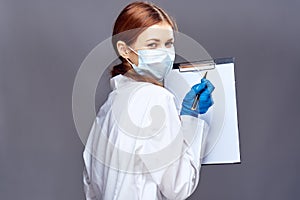 Young beautiful woman on gray background holds documents in medical dressing gown and mask, doctor, medicine