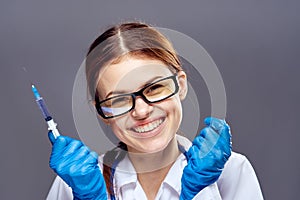 Young beautiful woman on a gray background in rubber gloves holds a syringe, doctor, medicine, hospital