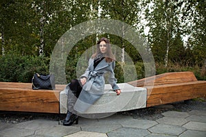 Young beautiful woman in a gray coat sitting on a bench in the autumn park