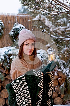 A young beautiful woman hangs a flashlight on a branch of a pine tree outside