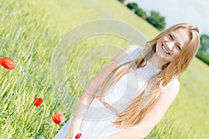 Young beautiful woman happy smiling & looking at camera walking in green wheat field on summer day