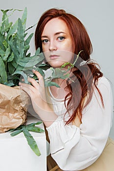 Young beautiful woman has red hair creative gold make up are posing in a studio with flowers