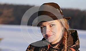 A young beautiful woman with a hat on her head portrait in a snowy landscape. Hunting clothes