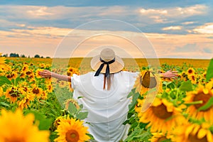 Young beautiful woman in hat rise hands to the susnet with clouds and field of sunflowers.