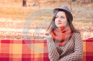 Young beautiful woman in a hat sitting on a bench in an autumn park