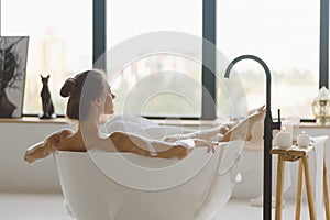 Young beautiful woman having bubble bath and looking at window.