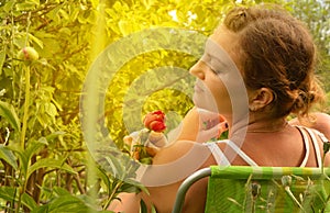 Young beautiful woman having fun sniffing flowers sitting on a chair in the garden on a summer day, beautiful female