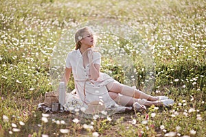 Young beautiful woman having picnic with tea in chamomile field