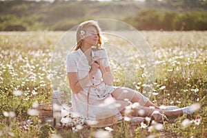 Young beautiful woman having picnic with tea in chamomile field