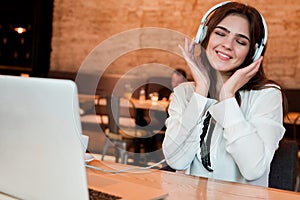 Young beautiful woman in headphones listening her favourite music from laptop while waiting her lunch in the cafe happy weekdays