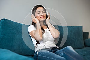 Young beautiful woman in headphones listening to her favourite music in the living room sitting on the sofa