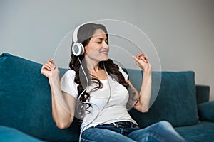 Young beautiful woman in headphones listening to her favourite music sitting on the sofa feeling happy