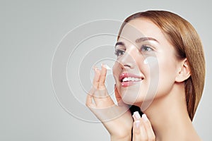 Young beautiful woman with healthy clear skin applying moisturizing cream on her face. Female face closeup