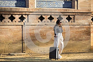 Young and beautiful woman, Hispanic, brown hair, with striped sweater, linen pants and sunglasses, standing, waiting by her