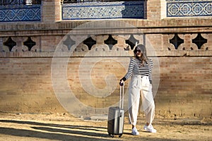 Young and beautiful woman, Hispanic, brown hair, with striped sweater, linen pants and sunglasses, standing, waiting by her