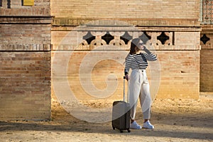 Young and beautiful woman, Hispanic, brown hair, with striped sweater, linen pants and sunglasses, waiting, talking on her cell