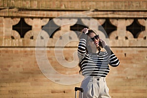 Young and beautiful woman, Hispanic, brown hair, with striped sweater, linen pants and sunglasses, waiting, talking on her cell