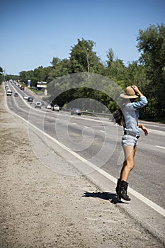 Young beautiful woman hitchhiking along a road