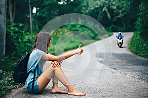 Young beautiful woman hitchhiking sitting on road
