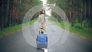 Young beautiful woman hitchhiking standing on the road with a suitcase on a table with an inscription SEA